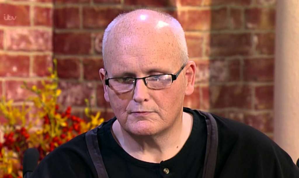 older man's face wearing optical glasses and black shirt